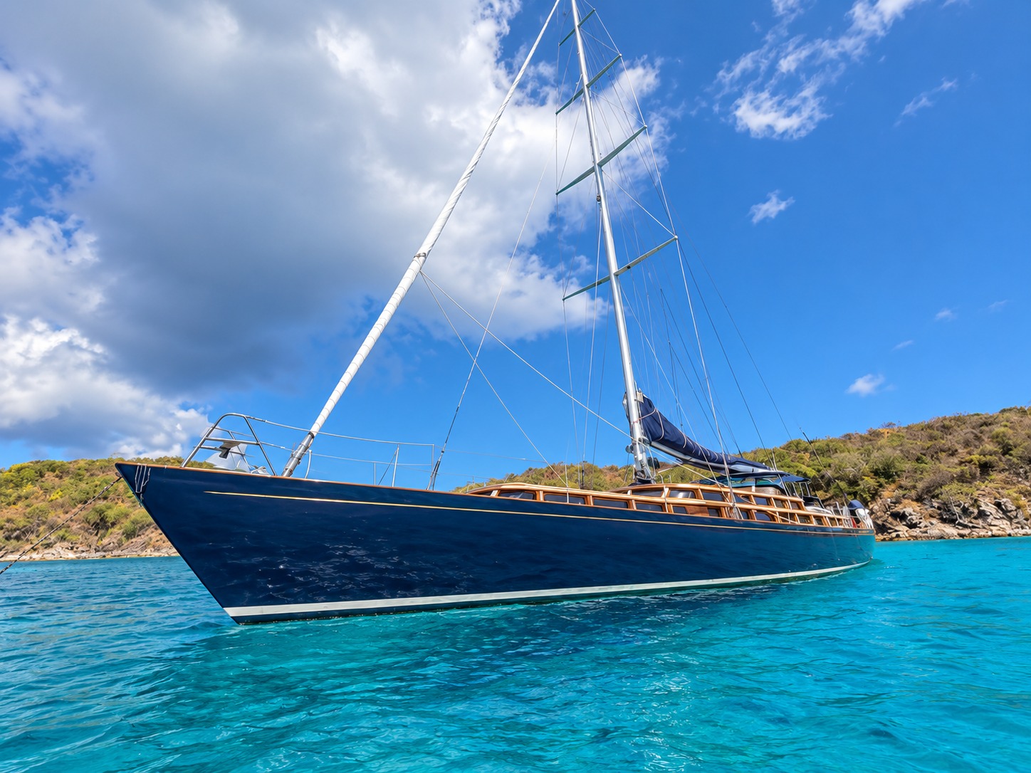 Lauren L at anchor, navy hull and varnished deckhouse over clear turquoise water