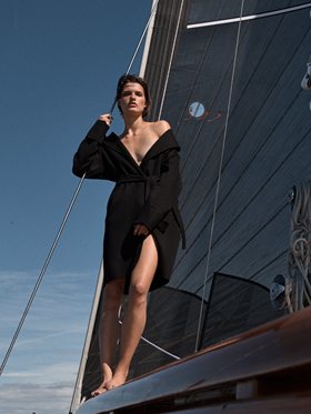 Standing on the coaming in a black coat against the dark sail